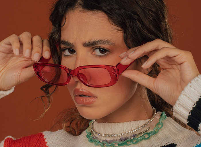 Person with red sunglasses and layered necklaces, exhibiting a retro vibe, potentially recalling high school trends.