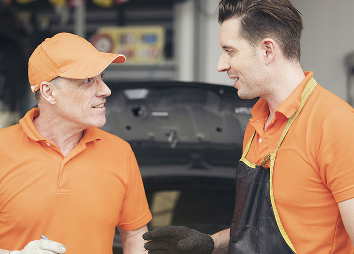 Two mechanics in orange shirts discussing work in a garage.