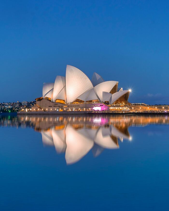 Sydney Opera House illuminated at night, reflecting on the water, showcasing unique architecture.