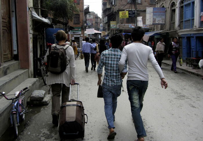 People walking down a bustling street with luggage in a foreign country, showcasing peculiar local customs.