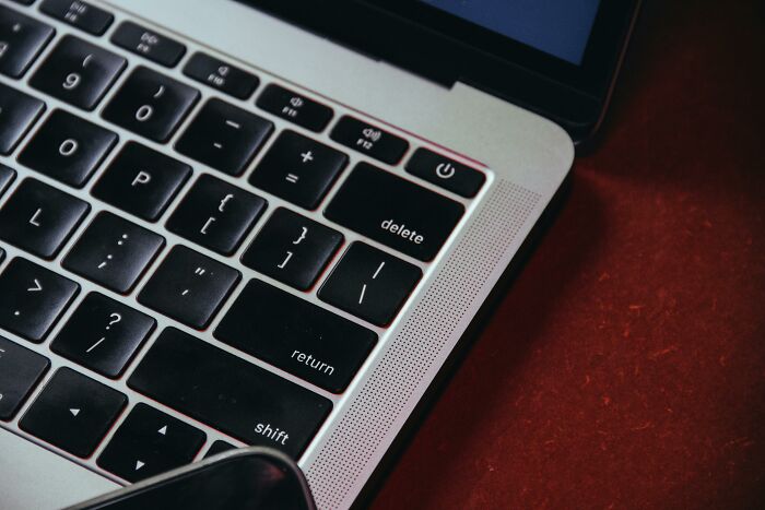 Close-up of a laptop keyboard on a red surface, focusing on the 'delete' key.