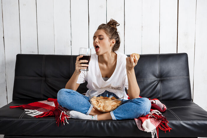Person on a couch with snacks and a drink, contemplating weight-loss tips for lifestyle changes.