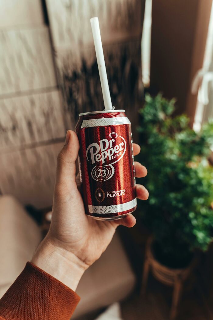 A hand holding a Dr. Pepper can with a straw, symbolizing a lifetime supply experience.