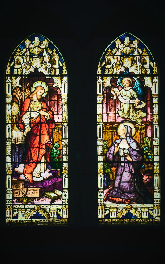 Stained glass window depicting religious figures in a church setting, with intricate designs and vivid colors.