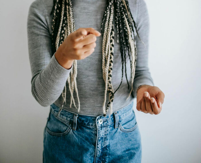 Person in a gray sweater and jeans gesturing with hands, likely in conversation, illustrating parent-teen dynamics.