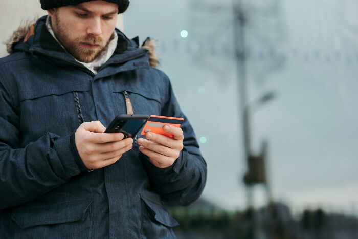 Man using a smartphone and holding a credit card, outdoors, demonstrating a smart way to slash household budgets.