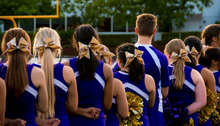 Cheerleaders with bows and uniforms at a sporting event, standing in a line on the field.