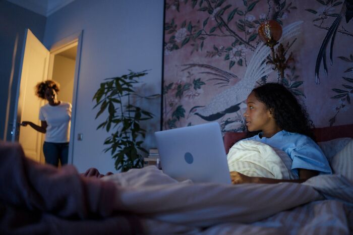 Teen on bed with laptop as parent enters room, representing parent-teen conflict.