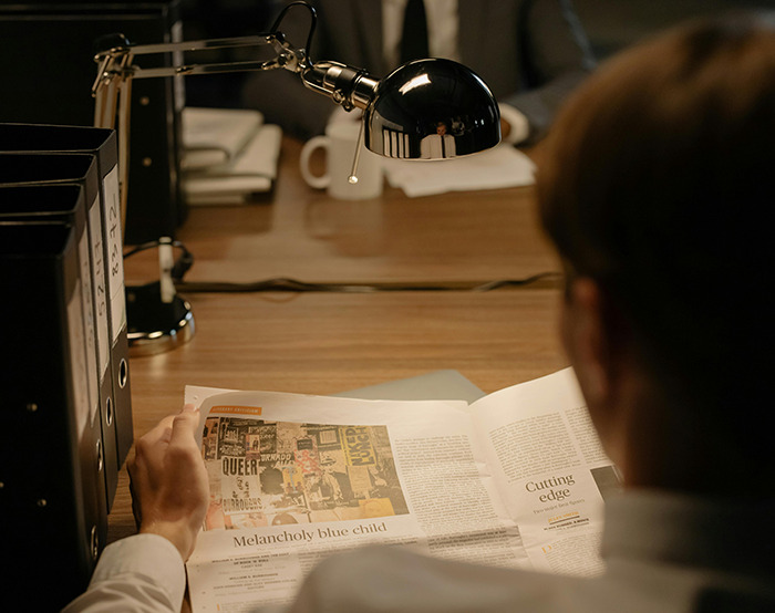 Person reading newspaper at desk under lamp.