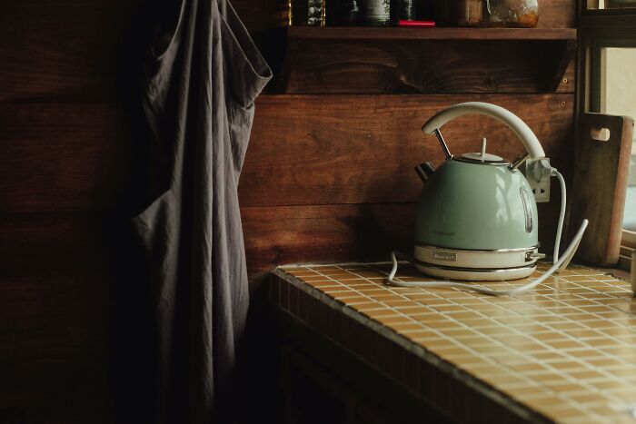 A kettle on a tiled kitchen counter with wooden shelves, representing items that improved lives.