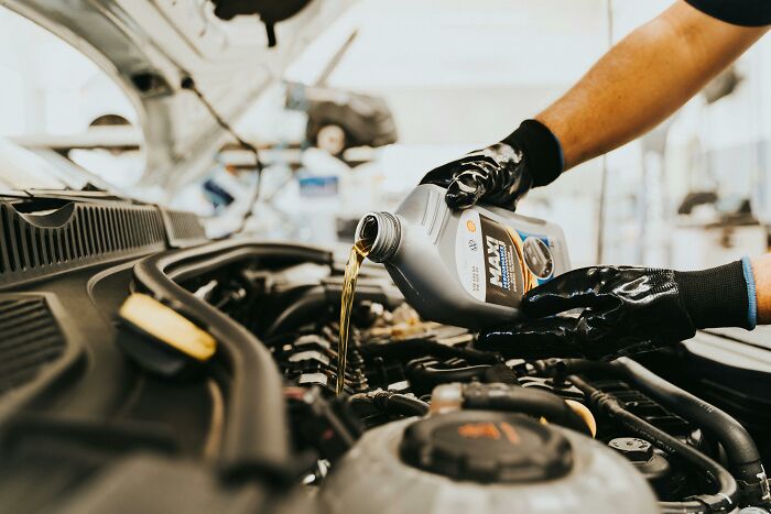 Person changing car oil to slash household budgets, wearing gloves in a garage setting.
