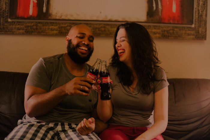 Couple enjoying sodas on a couch, smiling together, suggesting a relaxed lifestyle.