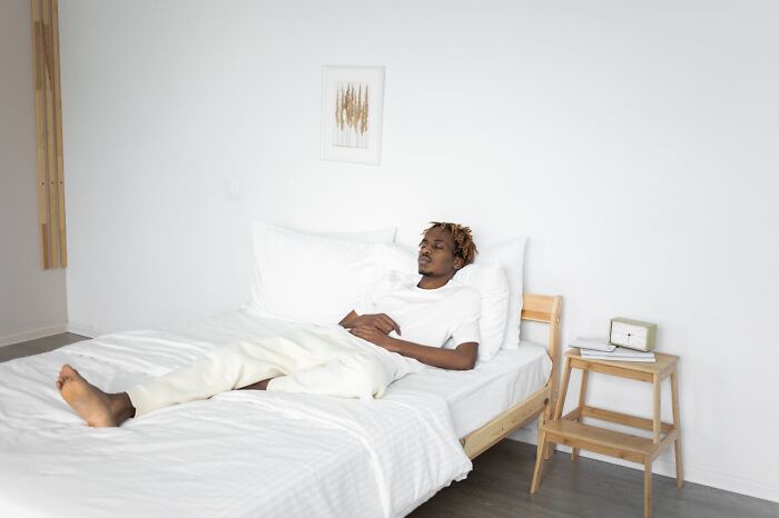 Man relaxing on a bed in a minimalist room, representing behaviors men shouldn't be judged for.