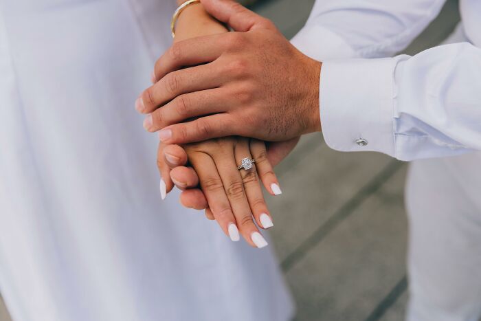 Hands of a forgiving loving partner gently holding each other with a focus on an engagement ring.