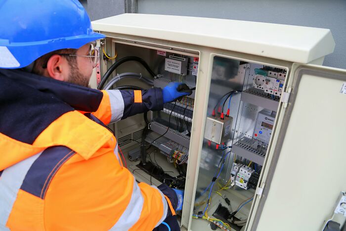 Technician in safety gear working on an electrical panel, focusing on space-saving installations.