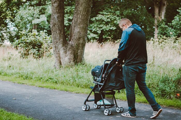 Man pushing a baby stroller in a park, illustrating activities men shouldn't be judged for doing.
