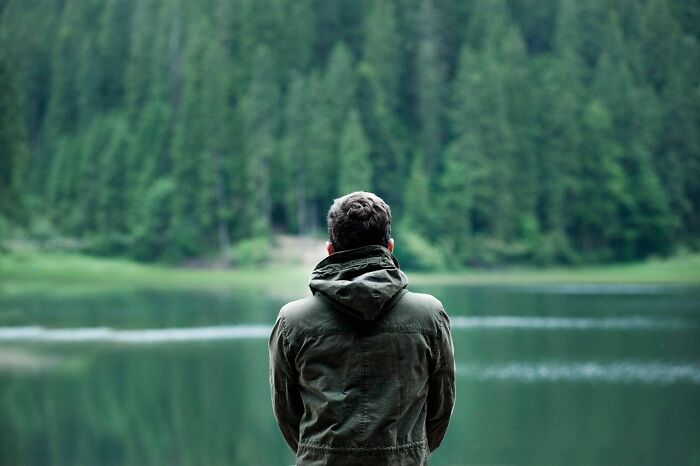 Man in jacket stands by a forest lake, representing freedom from judgment.