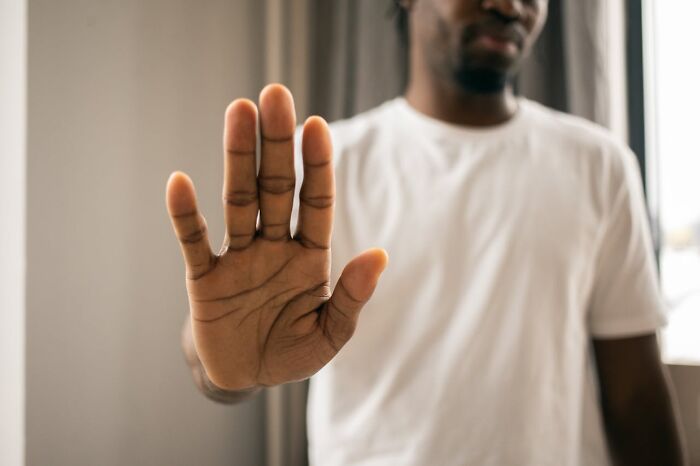 Man in a white t-shirt holds up his hand, suggesting a gesture on men's judgment.