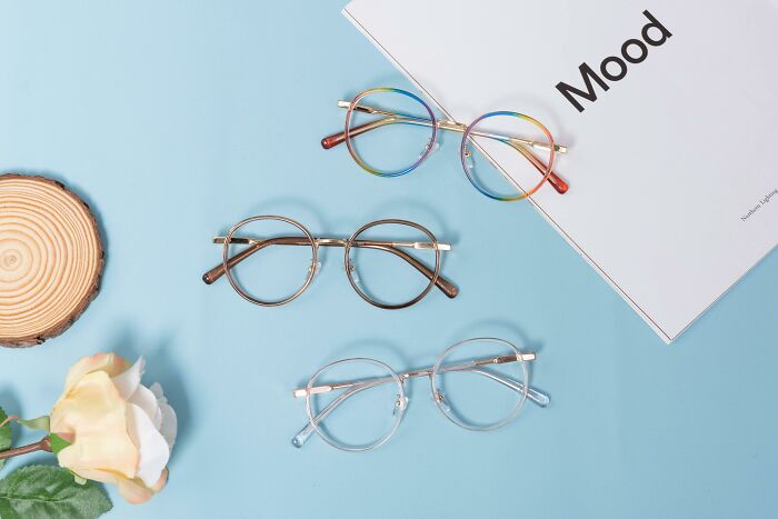 Three stylish glasses on blue surface, next to a book titled "Mood," symbolizing perception in the biggest scam narrative.