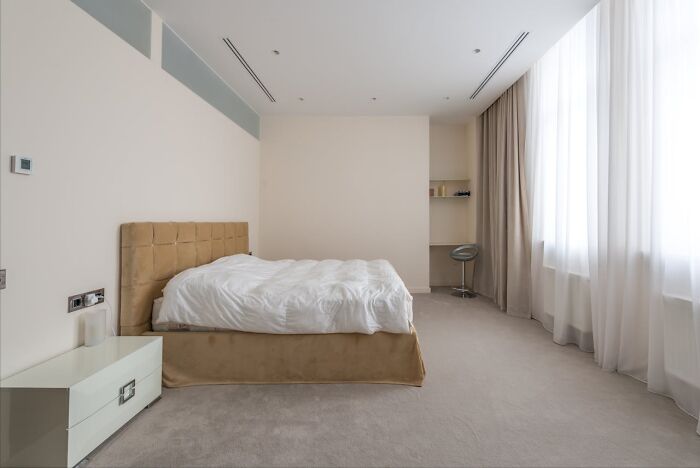 Minimalist bedroom with a beige bed and white linens, focusing on a clean and calm atmosphere.