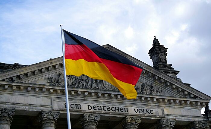 German flag waving in front of historic building under cloudy sky.