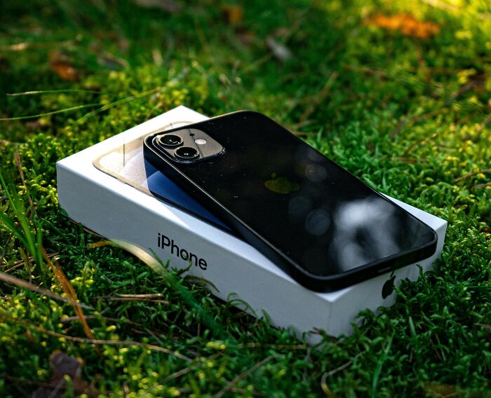 A black iPhone placed on its box, resting on grass.