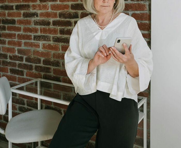 Parent using a smartphone, leaning against a brick wall, conveying potential communication gap with teens.
