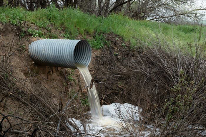 Drainpipe releasing water into a ditch, illustrating how everyday things might seem harmless but could be dangerous.