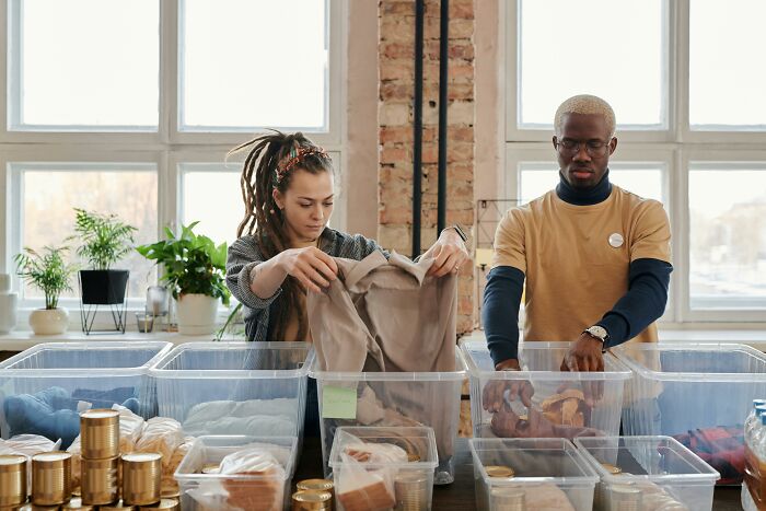 Two people sorting donations in a bright room, with bins of clothes and canned food, reflecting outdated financial stereotypes.