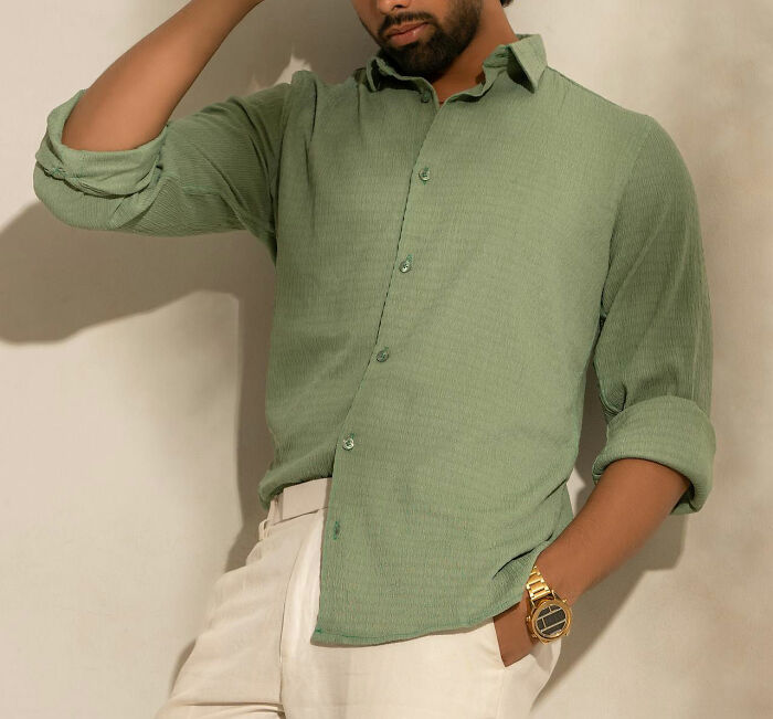 Man in a green shirt and beige pants leans casually, showcasing non-s****l charm.