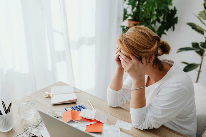 Stressed woman sitting at a desk with bills, symbolizing financial stress and scams.