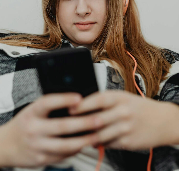 Person with long hair wearing headphones, using a smartphone while sitting comfortably, related to significant weight gain.