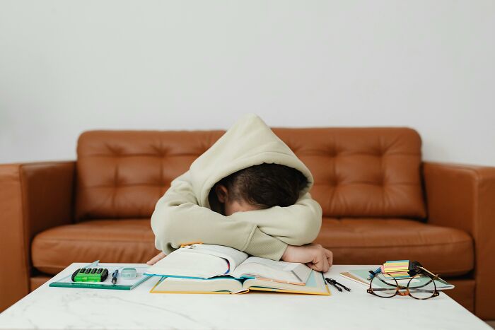 Person in a hoodie resting on a table, surrounded by open books and stationery, embodying trends resistance.