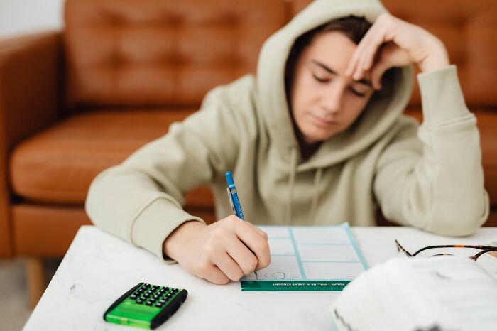 Teenager looking frustrated while doing homework, representing parent-teen conflicts.
