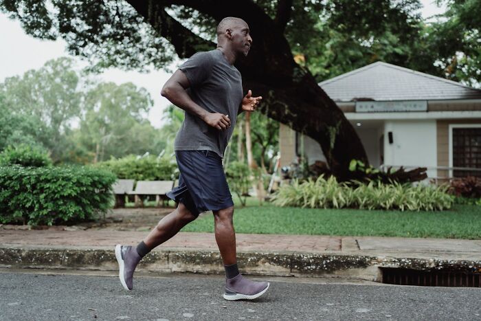 Man jogging in a park, wearing a gray shirt and shorts, focused on fitness despite weight gain challenges.