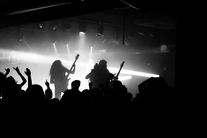 Silhouetted rock band on stage with cheering crowd, creating a mysterious atmosphere.