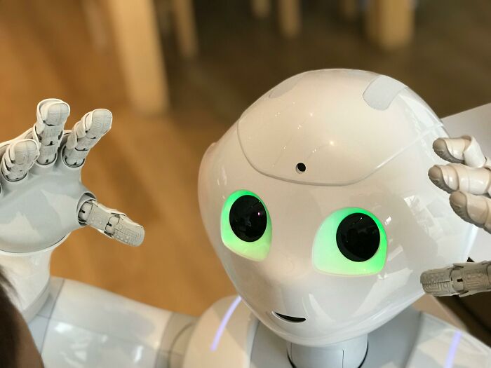 A humanoid robot with glowing eyes raises its hands in a playful manner.