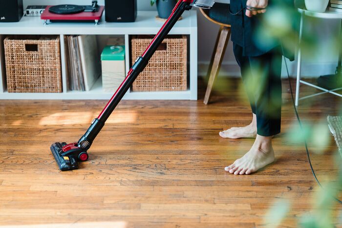 Person using a vacuum cleaner on a wooden floor, illustrating a space-saving purchase.