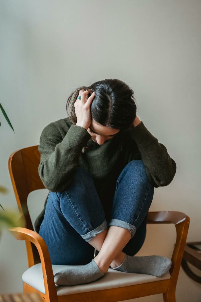 Teen looking distressed, sitting on a chair with head in hands, embodying conflict with parents.