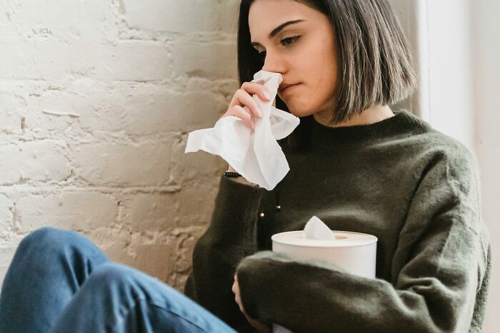 Person with tissues, symbolizing space-saving purchases, sitting by a brick wall in casual attire.
