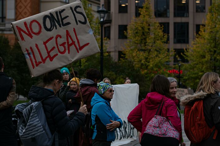 People at a protest holding a sign that reads "No One Is Illegal."