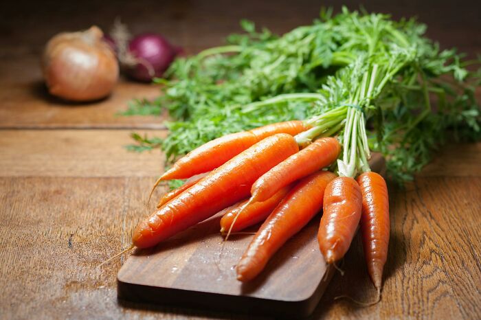 Fresh carrots with leafy tops on a wooden board, highlighting overlooked historical events and their impact on agriculture.