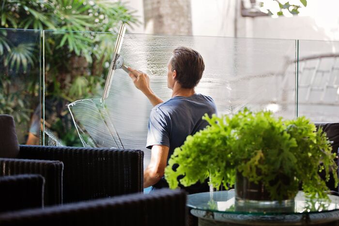 Man cleaning glass window outdoors, surrounded by plants; showing non-s****l things men do.