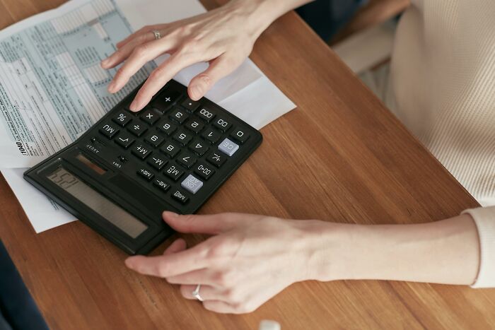 Millennials calculating finances on a wooden table with a black calculator and documents.