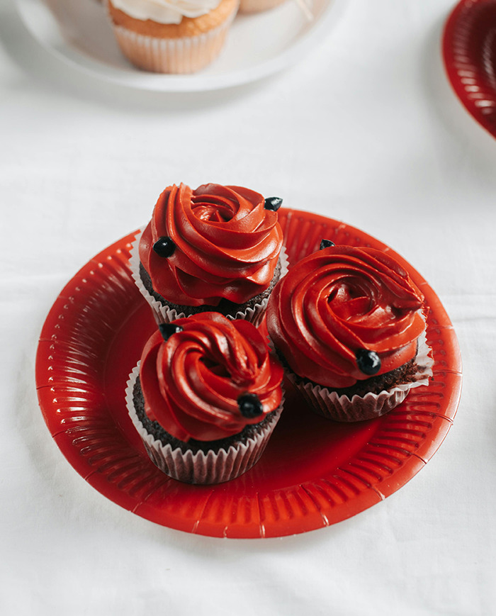 Three cupcakes with red frosting containing Red Dye No. 3 on a red plate.
