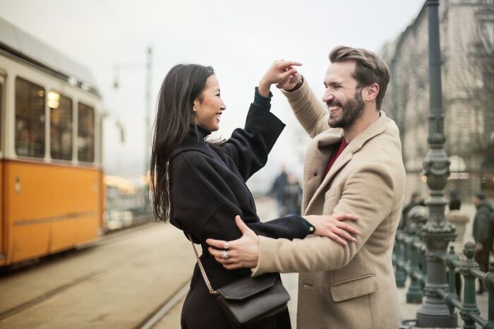 A man playfully dancing with a woman on a city street, showcasing non-s****l things men do that attract women.