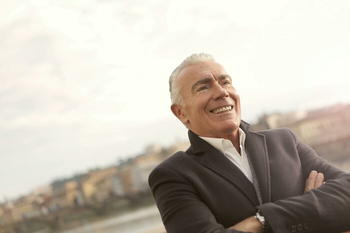 Smiling man in a coat with arms crossed, outdoors; related to teachers and crazy things in school.