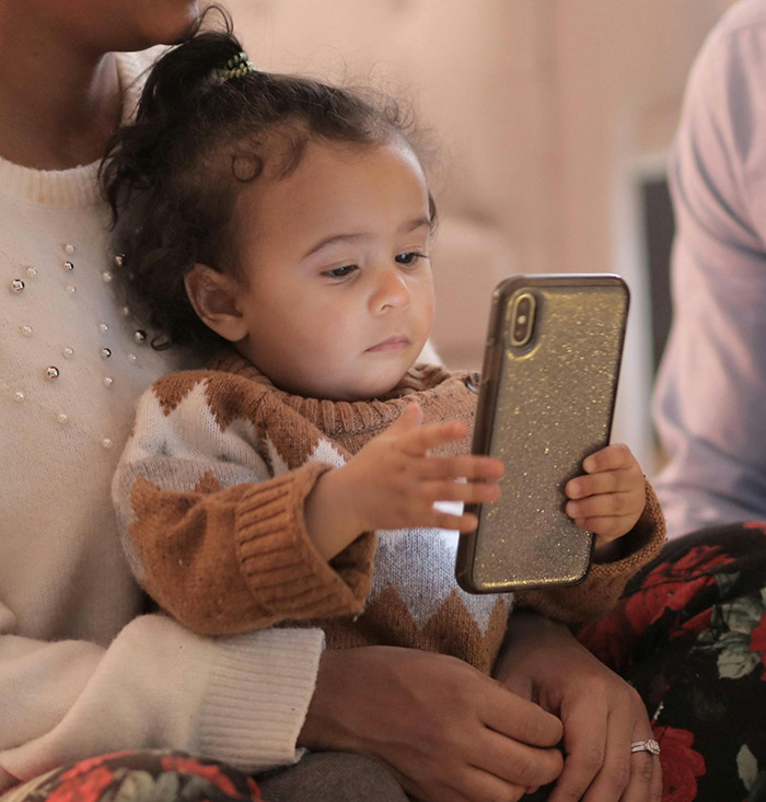 Baby intently looking at a smartphone while sitting in someone's lap.