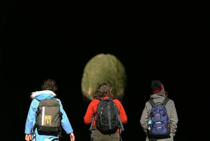 Three people with backpacks walking into a dark tunnel, possibly exploring weird unsolved mysteries.