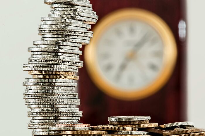 Stack of coins in front of a blurred clock, symbolizing outdated financial stereotypes and the passage of time.